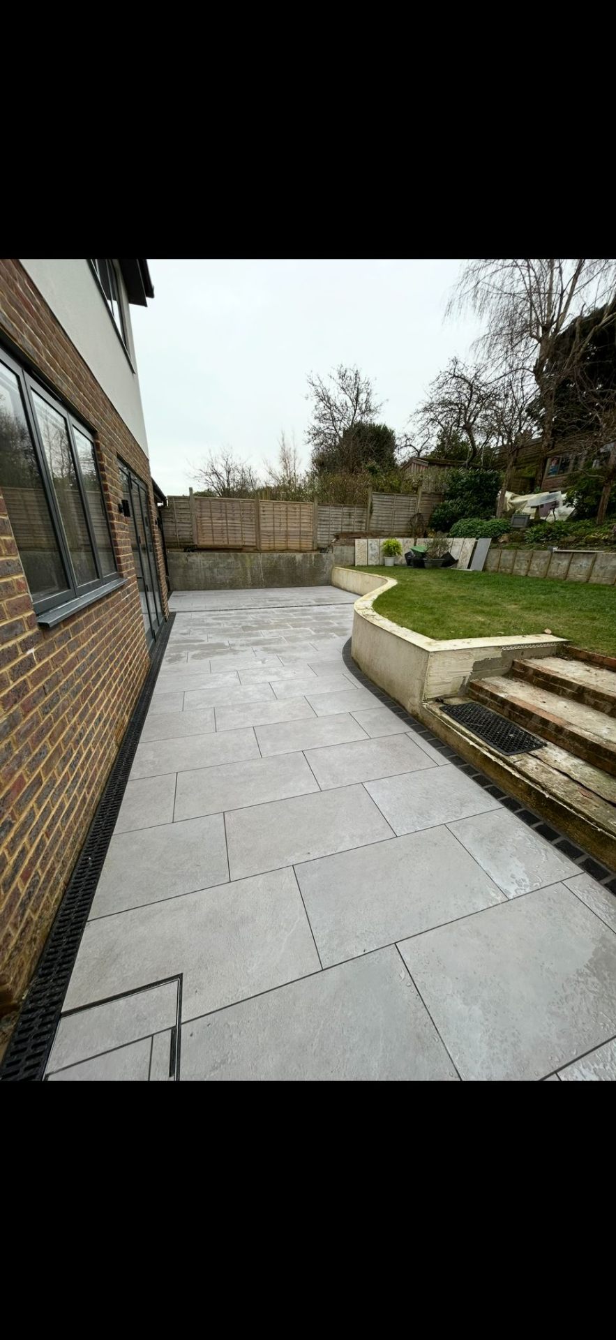 Grey porcelain patio with retaining wall and new lawn by Burton Builds